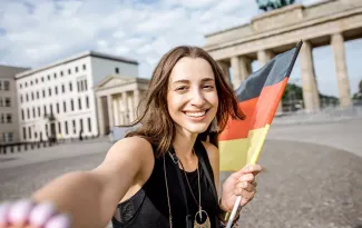 Lachende Studentin vor dem Brandenburger Tor mit Deutschlandfahne