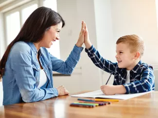 Ergotherapeutin macht "High Five" mit einem Jungen am Schreibtisch