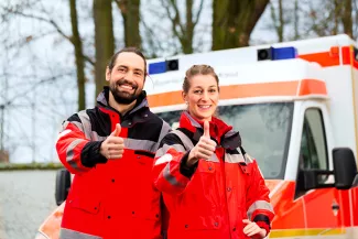 Karriere machen im Rettungsdienst mit dem Fernstudium Krisenmanagement Mann und Frau in DRK-Uniformen mit Daumen hoch vor einem RTW